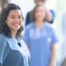 A woman in scrubs smiles with a team behind her, representing the joy that can come from a career as an OT, as Occupational Therapy Month promotes.